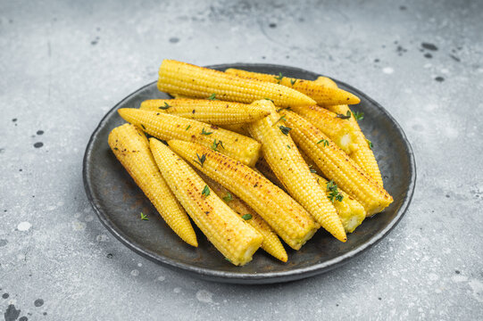 Golden roasted baby corn seasoned with thyme served on ceramic plate over stone background cooked vegetable dish with copy space