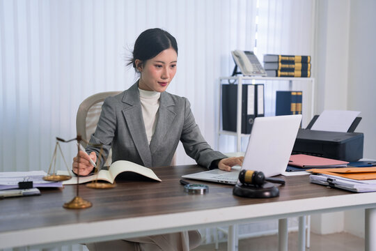 Asian female lawyer writing legal document at office desk with gavel scale law books computer professional attorney working on case study legal consultation