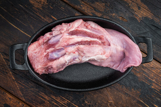 Fresh raw pork tongue meat cut with thyme shown in skillet top view on rustic dark wood backdrop for slow cooking