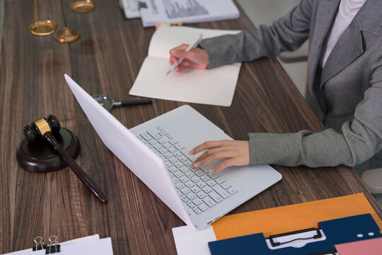 professional lawyer attorney working laptop computer writing legal document notes consulting client meeting law firm office reviewing case files at modern desk