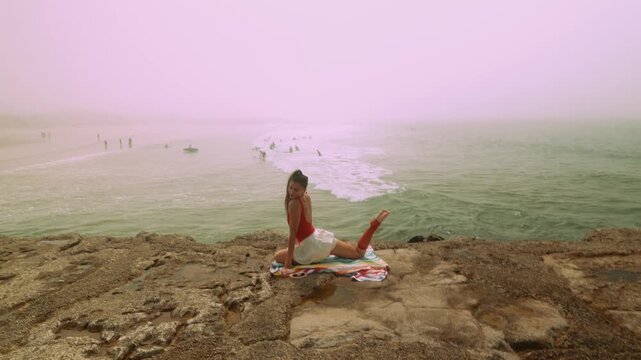 Relaxed lady in swimsuit gazes at distant surfers and gentle sea