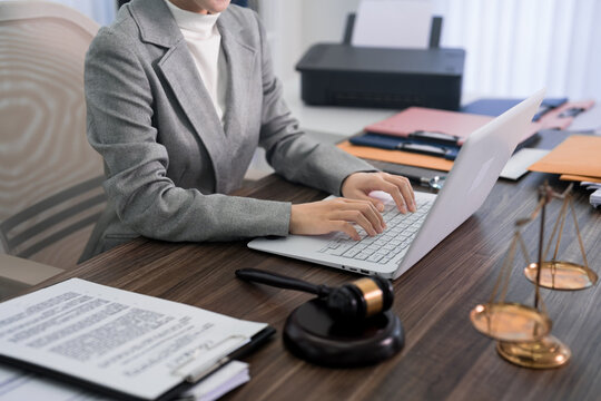 professional Asian woman lawyer using laptop computer typing legal document working on case research with gavel and justice scale at law office desk legal