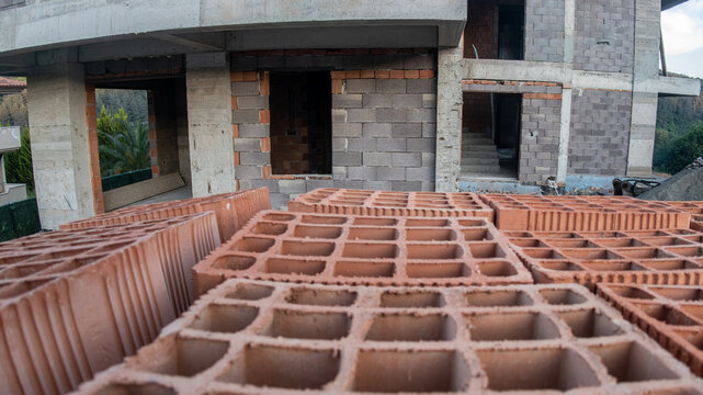 Close-up of hollow red clay bricks in the foreground of a building construction site with a concrete and briquette structure in progress. Real estate development.