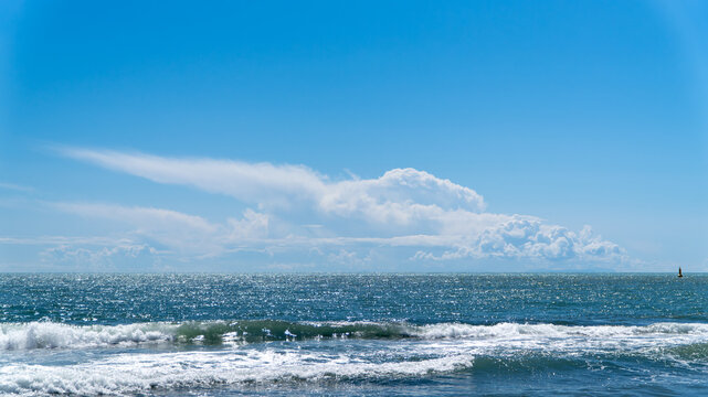 Wide sea horizon with blue water and white breaking waves under a clear sky with a large white cloud. Minimalist coastal landscape in Dalaman, Turkey.