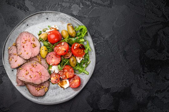 Roast beef salad with medium rare beef slices arugula tomatoes olives and cheese on dark stone background top view copy space