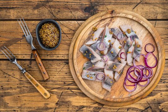 Marinated salted herring fish pieces with spices on round wooden board. Nordic preserved seafood top view with copy space.