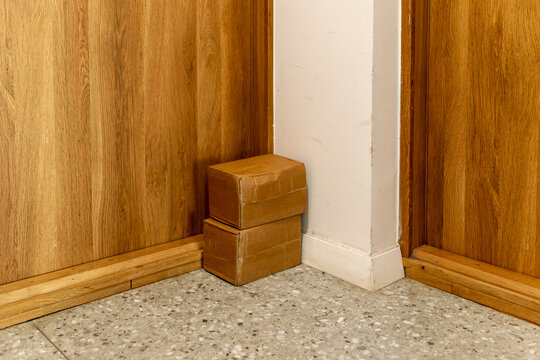 Two small cardboard parcels stacked in a hallway corner between wooden doors. Useful for delivery, shipping, online order, moving, package, storage and home interior concepts.