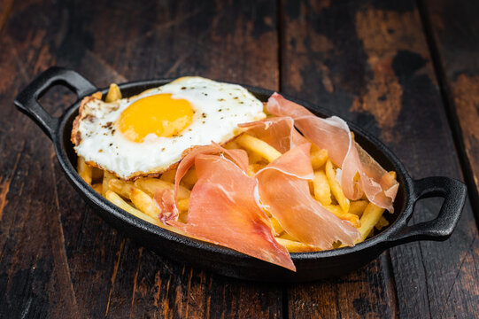 Huevos rotos Spanish cuisine with fried broken eggs potatoes and jamon in cast iron skillet on wooden table