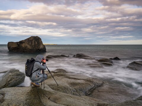 Photographer with tripod on smooth rocks by the sea, Utakleiv, Vestv&aring;g&oslash;ya, Lofoten, Norway