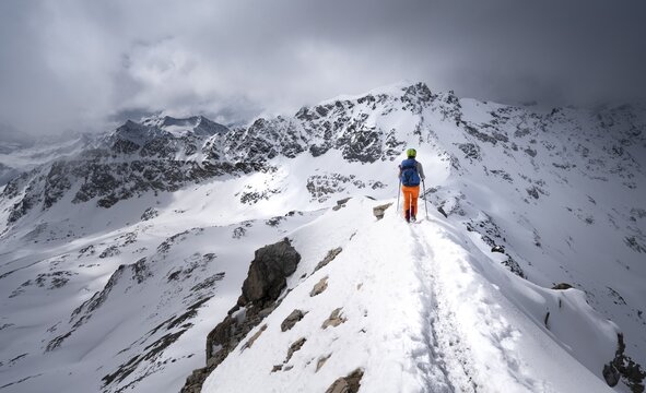 Mountaineer descending the narrow ridge of Piz Laviner, view of mountain panorama in wintry mountain landscape with dramatic clouds, Grisons Haute Route, Albula Alps, Rhaetian Alps, Grisons, Eastern Switzerland, Switzerland