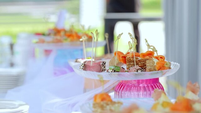 Elegant pink glass stands displaying gourmet salmon canapes, crackers, and appetizers at catered event with blurred background suggesting refined dining atmosphere