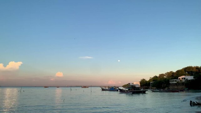 4K serene seascape at Tanjung Lesung Beach, Banten, Indonesia, featuring calm rippling water, fishing boats, moonlit sky, and coastal scenery. Ideal for travel, tourism, nature, relaxation, and vacati
