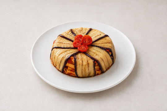 Traditional Italian baked pasta timbale with eggplants and cherry tomatoes on a neutral background