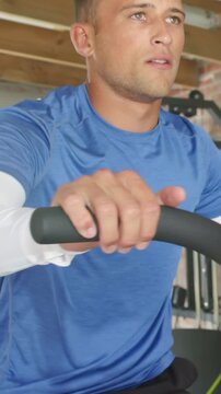 Vertical video: Gripping padded bars man in blue tee over white sleeve training crank in home gym