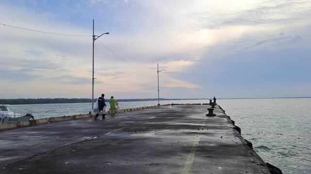 PAMEKASAN, INDONESIA - JANUARY 10, 2026: Traditional fisherman throwing a casting net into the sea from a concrete pier in Madura, Indonesia. This cinematic footage captures the skillful technique.