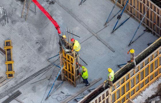 Construction site team using concrete pump truck hose to fill wall formwork