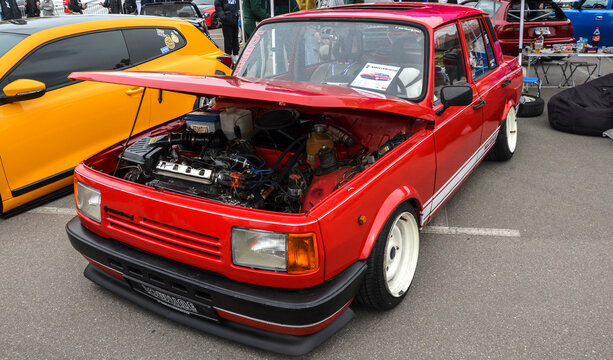 Bright red Wartburg 353 sedan with white racing stripes and matching white steel wheels at a car festival