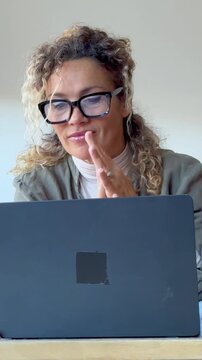 Satisfied mature businesswoman with curly hair and glasses finishing her work, stretching her neck, and closing her laptop at the office desk with a smile and relaxed expression
