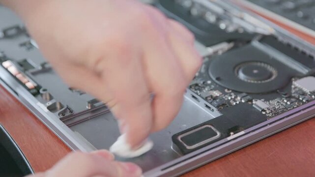 The process of thoroughly cleaning the inside of a metal laptop case with an alcohol wipe before installing the battery.
