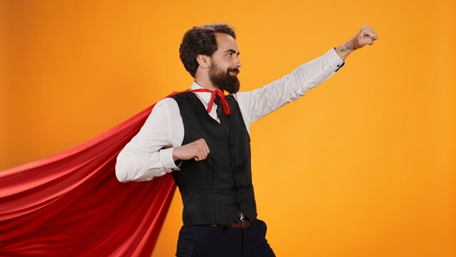 Powerful hero butler posing with red cape against yellow background, dedicated to serve consumers at fine dining restaurant. Concept of strong confident superhero character, luxury catering.