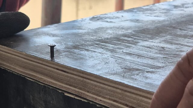 Slow motion close-up of hitting a steel nail with a hammer into a wooden formwork structure, detail of carpentry work.