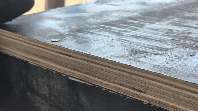 Close-up shot of a carpenter driving a metallic nail into a wooden shuttering panel with a hammer on a construction site.