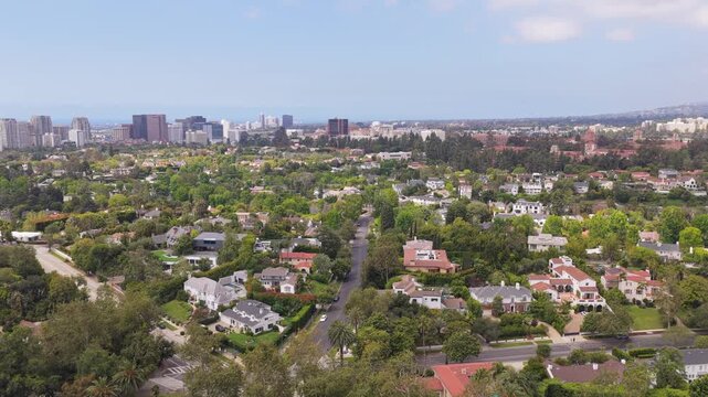Exclusive Beverly Hills residential district with opulent mansions and green gardens flying toward Century City's modern skyline in sunny Southern California