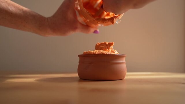 women serving a homemade red bell pepper dip into a bowl