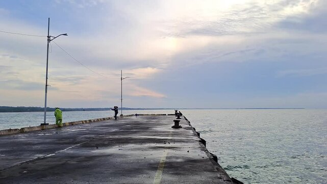 PAMEKASAN, INDONESIA - JANUARY 10, 2026: Traditional fisherman throwing a casting net into the sea from a concrete pier in Madura, Indonesia. This cinematic footage captures the skillful technique.