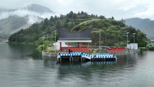 Samosir Regency, Indonesia - 25 February 2025: Aerial view of Sibea Bea hill with a traditional Batak pavilion on a pier overlooking Lake Toba, surrounded by misty mountains.
