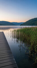 Obraz premium Wooden pier on a calm lake with reeds at sunrise, symbolizing peace, nature, and tranquility, perfect for travel or relaxation themes