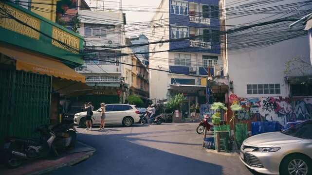 Bangkok urban alleyway showcasing tangled electrical wiring, street art, and daily life in Thailand with pedestrians and traffic