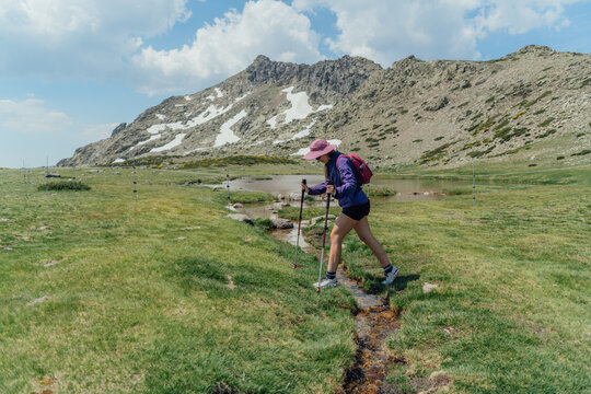 Woman with trekking poles crosses a mountain stream