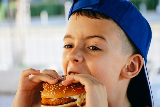 Young boy in a blue cap eating a burger