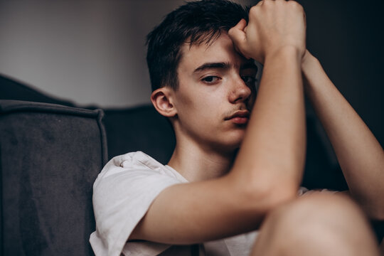 A pensive teenage boy sits alone at home