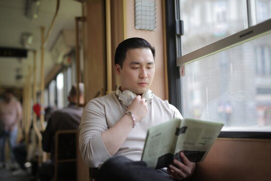 Young Asian man reading a newspaper on the morning commute