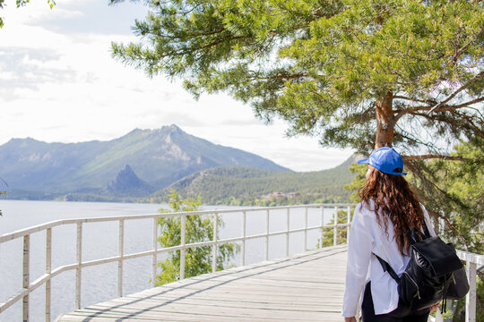 Back view of a young woman admiring the panoramic view of Lake Borovoe, mountains and pine forest in Burabay National Park, Kazakhstan. Travel, nature and outdoor adventure concept.