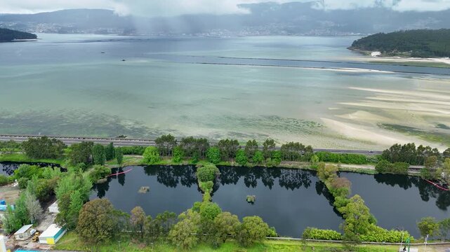 Aerial view of Biofabrica de Ence surrounded by green trees and the Ria de Pontevedra estuary under a cloudy sky in Pontevedra, Pontevedra, Spain.