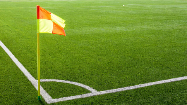 Iconic red corner flag standing on the edge of a professional football pitch, fluttering in the wind as the game begins, representing precision and the traditional rules of the beautiful game.