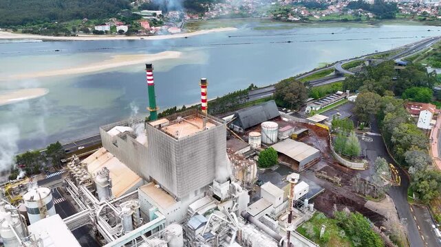 Aerial view of the Biofabrica de Ence pulp mill with smoking chimneys and industrial structures near the estuary in Pontevedra, Pontevedra, Spain.