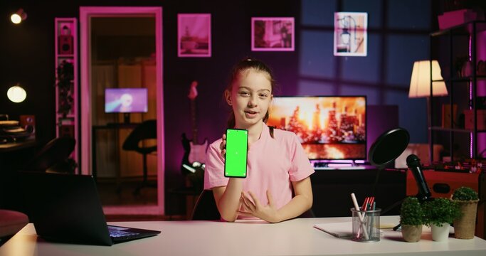 Cute kid filming internet show, promoting green screen tablet received from sponsoring brand. Little girl does influencer marketing, urging followers to purchase chroma key device