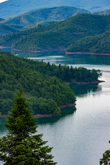 Fototapeta premium Scenic aerial view of Lake Plastira in Greece, featuring lush green forested hills reflecting on calm turquoise water. Beautiful natural landscape photography for travel and nature concepts.