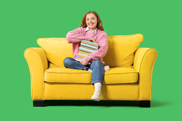 Obraz premium Young woman with stack of books sitting on sofa against green background