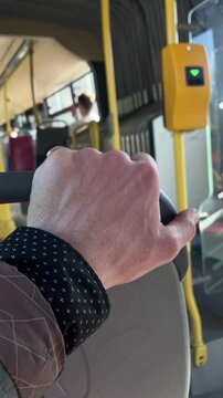 White hand gripping bus seat during morning commute, closeup of knuckles and veins, yellow validator and pole in background, city transit interior