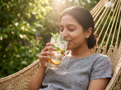 South Asian Woman Taking a Refreshing Sip of Iced Tea with Closed Eyes in Hammock - Summer Relaxation