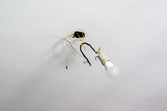 A electric bulb hangs from wires coming out of the ceiling, unfinished construction