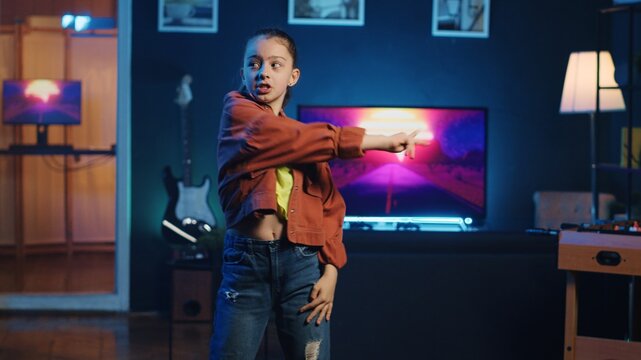 Excited youngster doing viral dance social media content while listening to popular hit song. Joyful kid recording dancing video for her internet audience on latest viral music