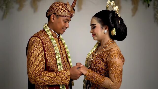 Romantic Indonesian Newlyweds in Traditional Javanese Gold Wedding Costumes Looking at Each Other