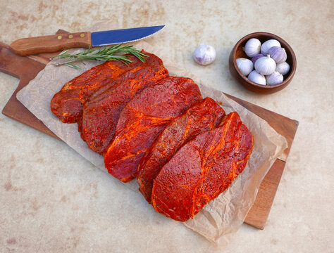 Marinierte Schweinenackensteaks zum Grillen auf Holzbrett mit Knoblauch.