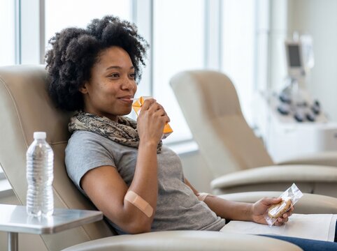 Diverse Woman Smiling and Resting with Snack after Blood Donation - Medical Recovery